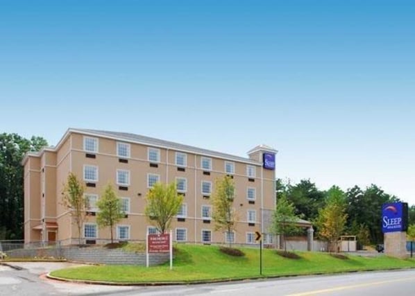 Un hôtel à plusieurs étages, à la façade beige, avec une enseigne indiquant qu’il s’agit d’un Sleep Inn Express, et un ciel bleu clair en arrière-plan.