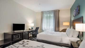 A hotel room with two beds, a desk with a flat-screen TV, a chair, and a desk lamp.