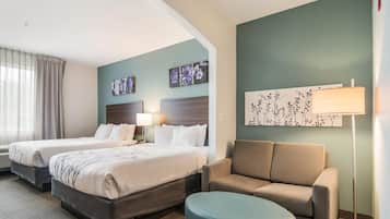 A hotel room with two beds, a sofa, a round ottoman, and artwork on the walls.