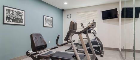 A fitness room with exercise equipment, a clock, and framed pictures on the wall.