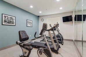 Een fitnessruimte met trainingsapparatuur, een klok en ingelijste foto's aan de muur.