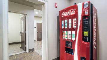 A Coca-Cola vending machine in a hallway with a door leading to another room.