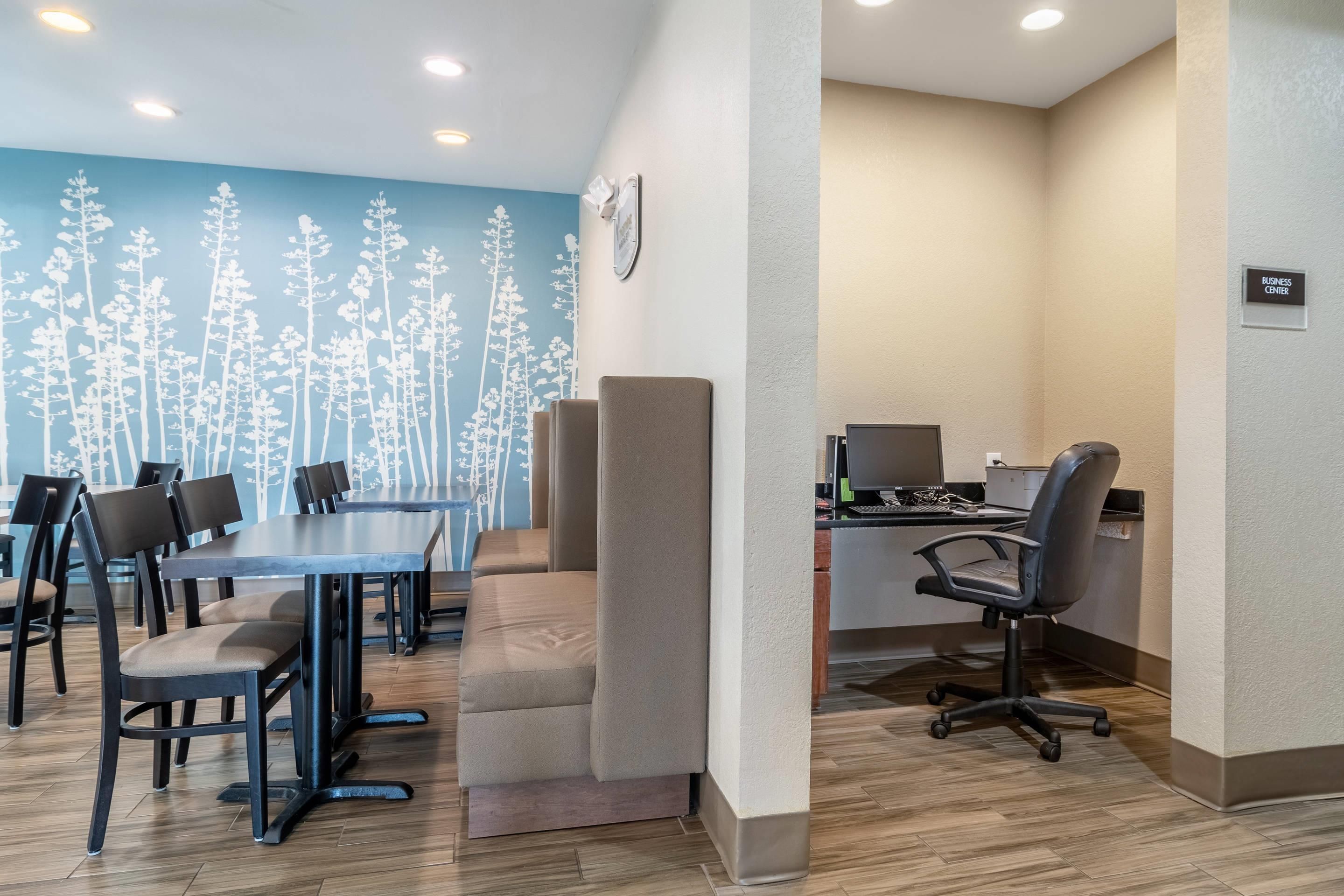 A conference room with a long table, multiple chairs, a computer desk with a monitor, and a wall with a tree pattern.