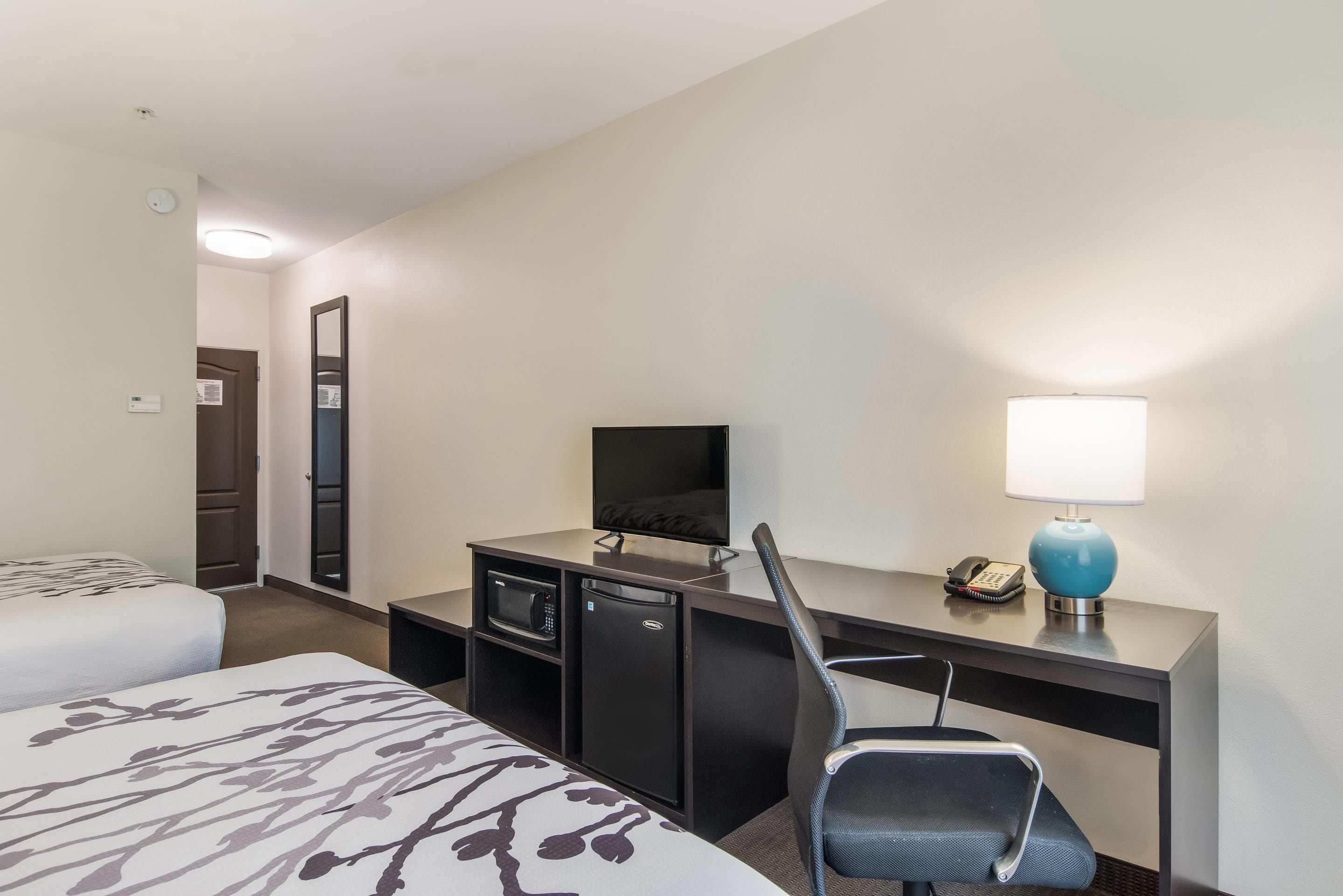 A hotel room with a bed, a desk with a computer, a chair, a desk lamp, and a telephone.