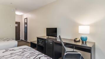 A hotel room with a bed, a desk with a computer, a chair, a desk lamp, and a telephone.