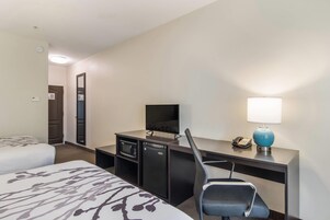Quarto de hotel com cama, escrivaninha, computador, cadeira, luminária e telefone.