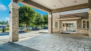 A covered outdoor area with a brick building, a tiled walkway, and a parking lot with cars. - Sleep Inn and Suites at Kennesaw State University (Kennesaw)