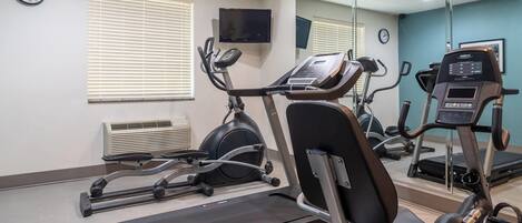 A gym with cardio equipment, a TV, and a clock on the wall.