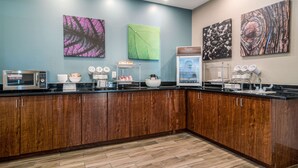 A modern kitchen with wooden cabinets, a microwave, a coffee station, and artwork on the walls. - Sleep Inn and Suites at Kennesaw State University (Kennesaw)