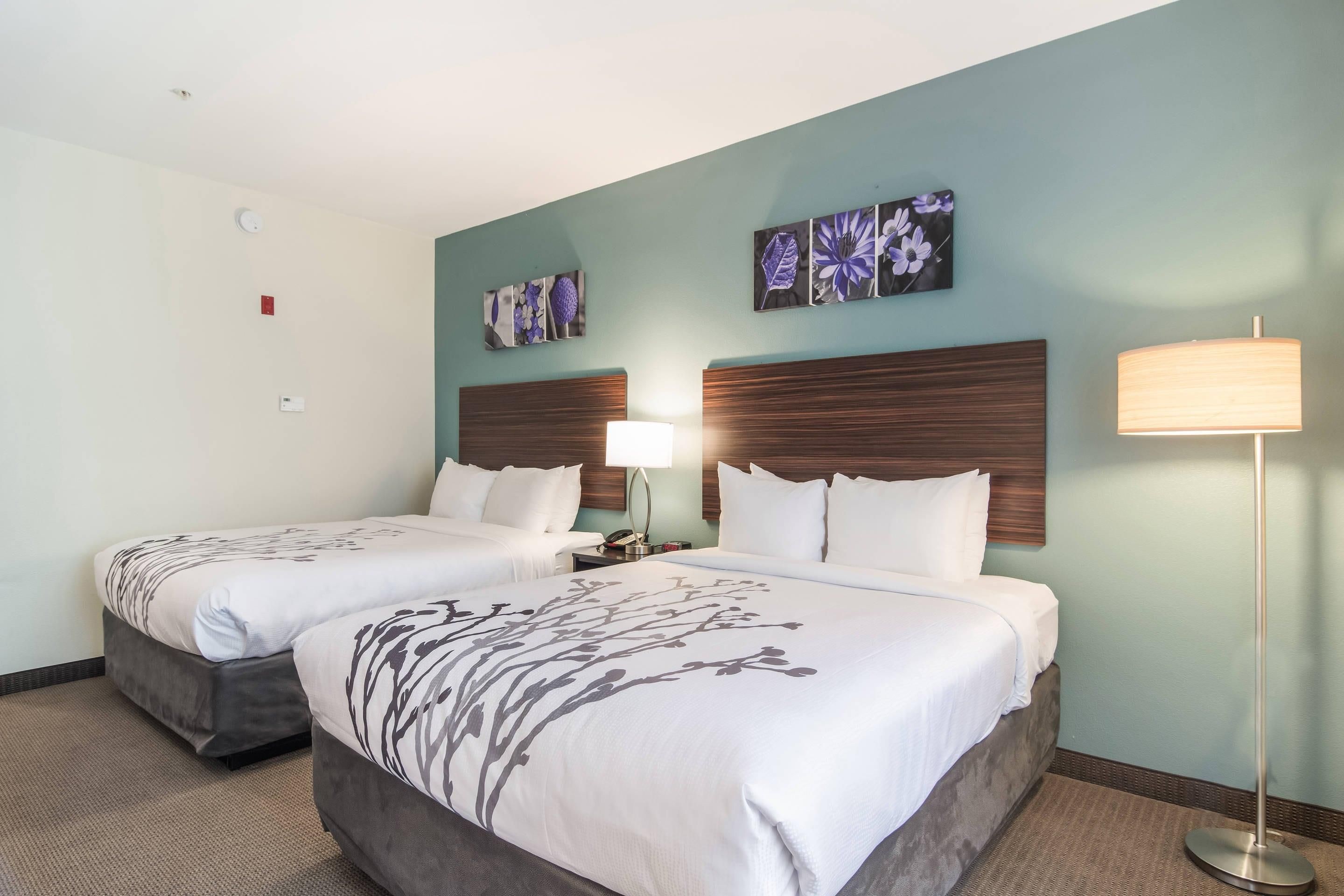 A hotel room with two beds, a nightstand, a lamp, and wall art.
