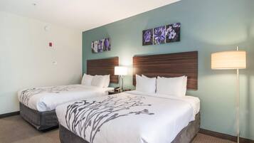 A hotel room with two beds, a nightstand, a lamp, and wall art.