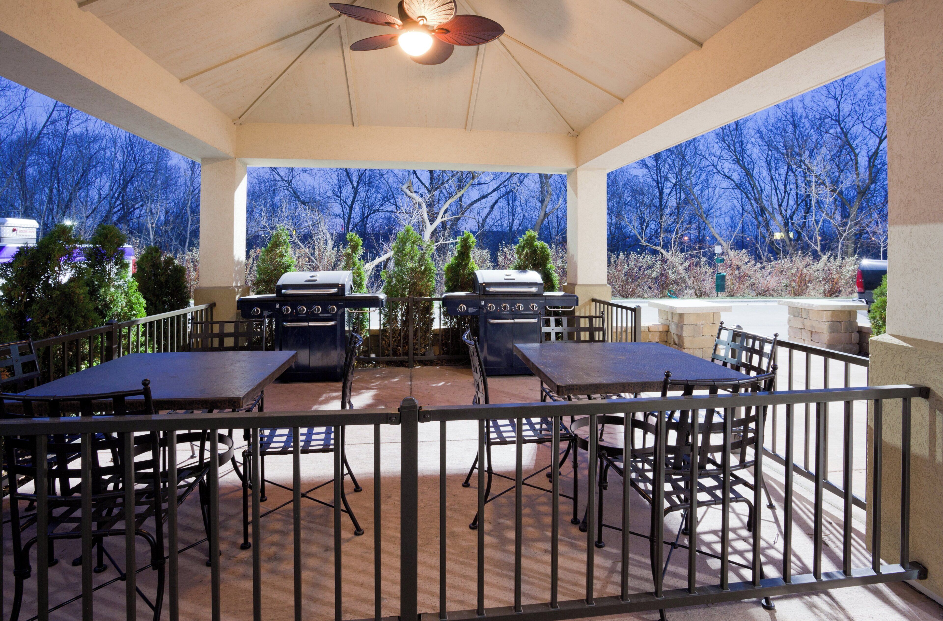 An outdoor patio with a ceiling fan, two barbecue grills, and a table with chairs.