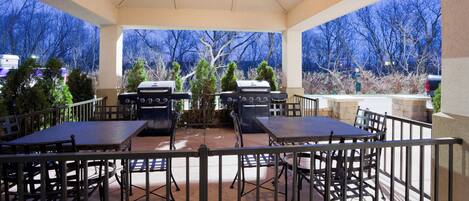 An outdoor patio with a ceiling fan, two barbecue grills, and a table with chairs.