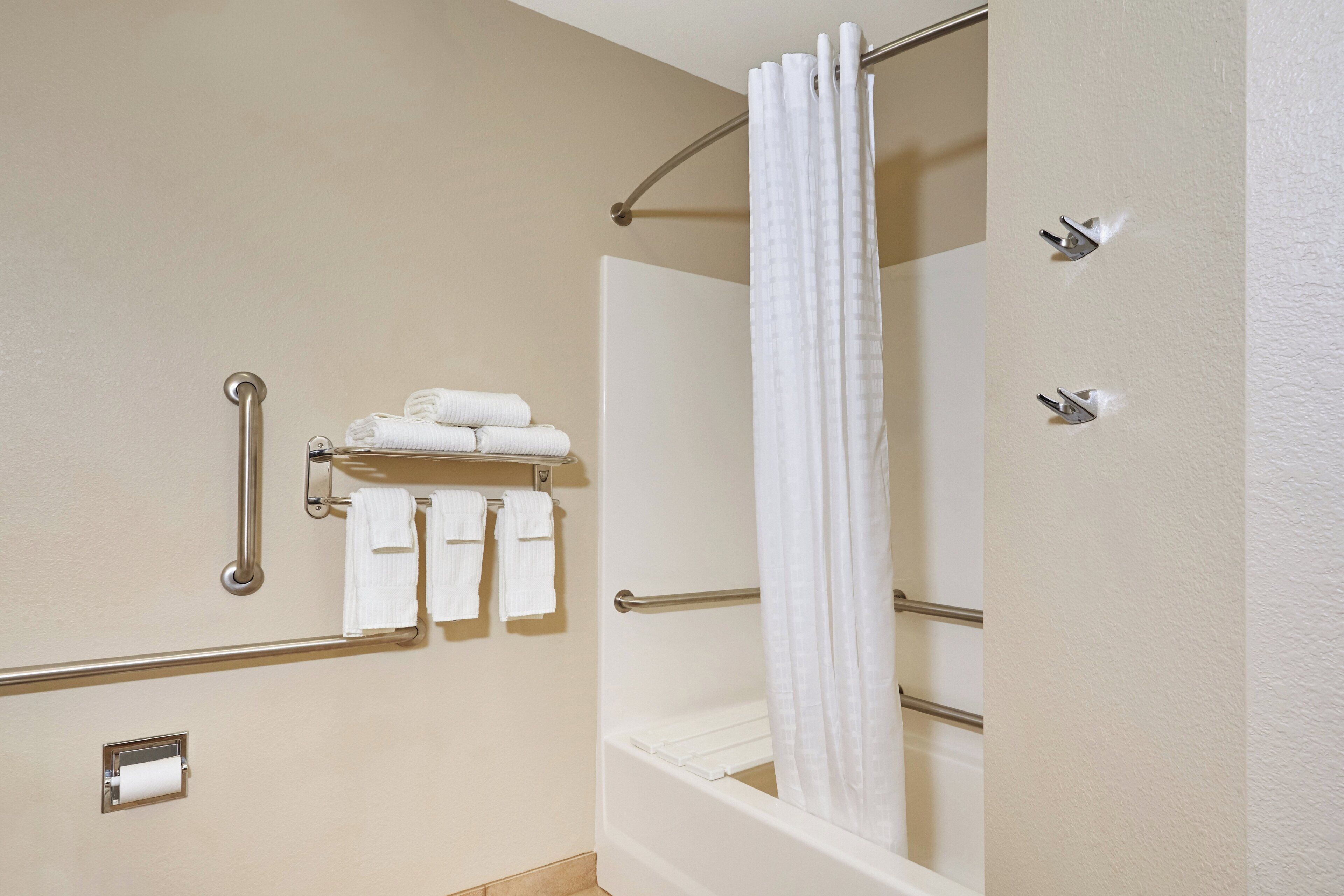 A bathroom with a shower, a towel rack with towels, a handrail, and a toilet paper holder.