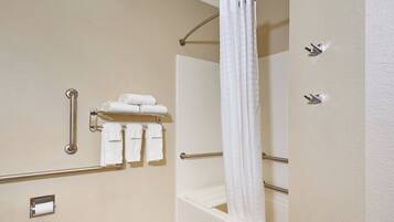 A bathroom with a shower, a towel rack with towels, a handrail, and a toilet paper holder.