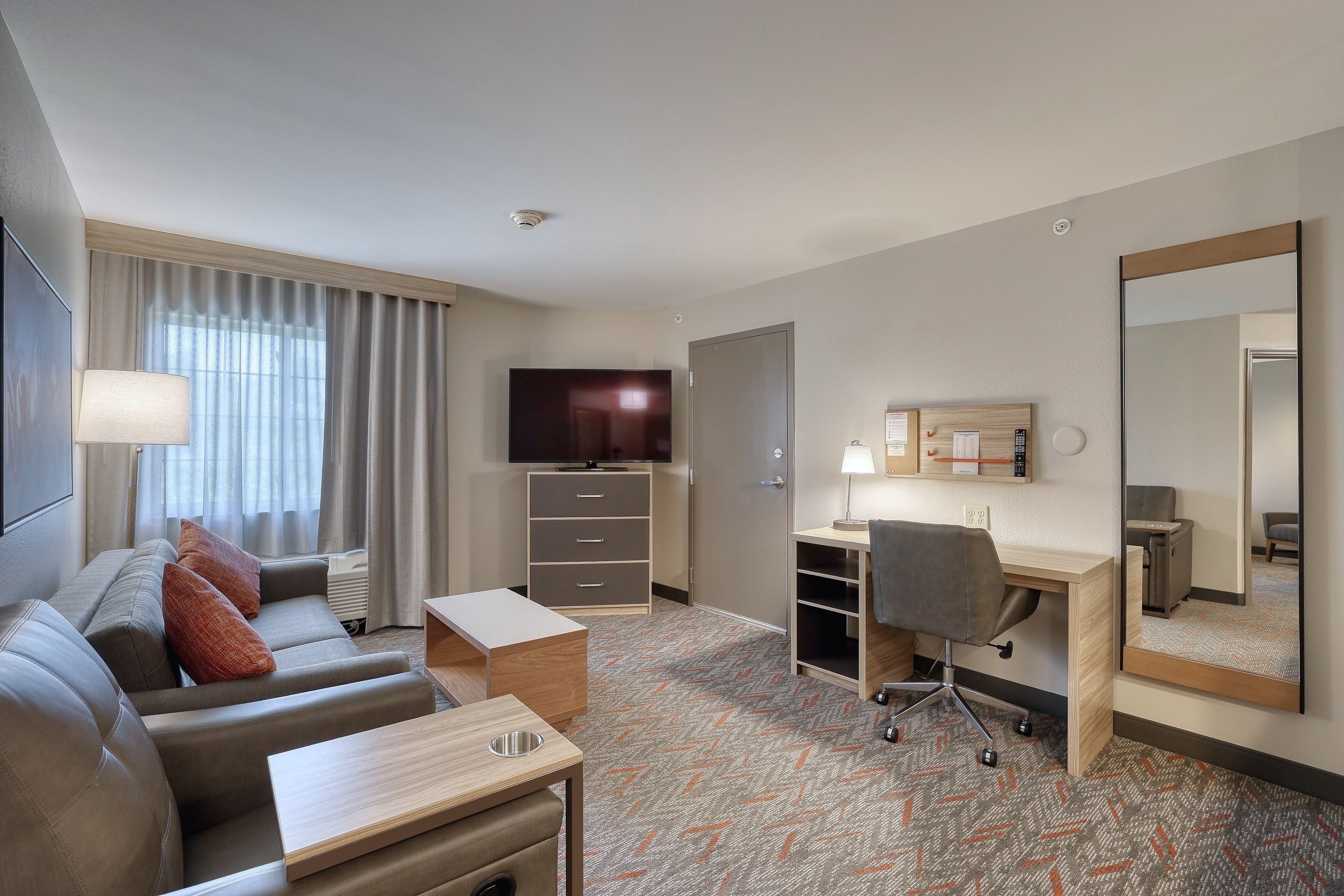 Habitación de hotel con sofá, escritorio y un espejo grande.