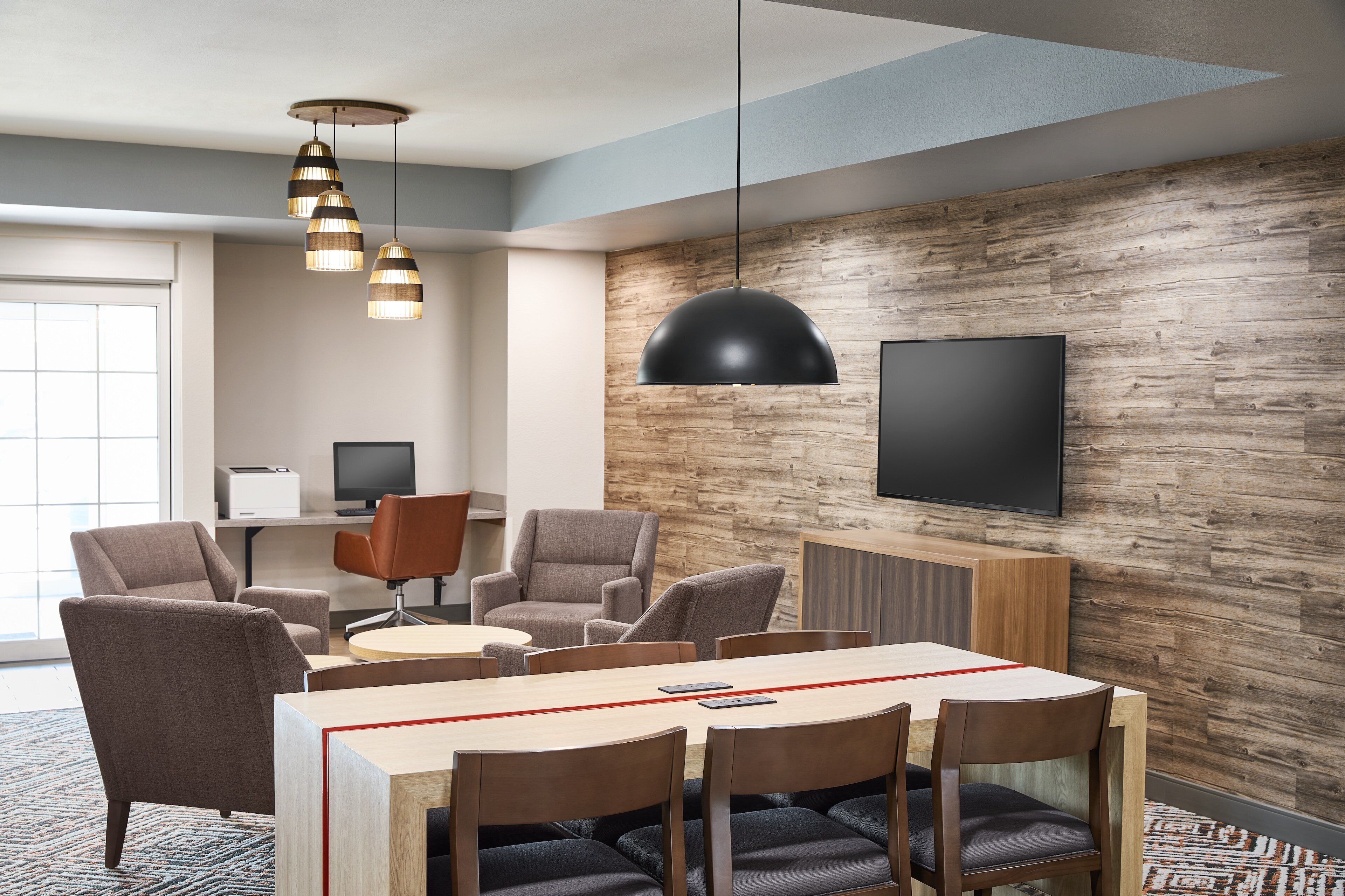 Una sala de reuniones moderna con pared de madera, un televisor de pantalla plana grande y una zona de comedor con sillas y una mesa.