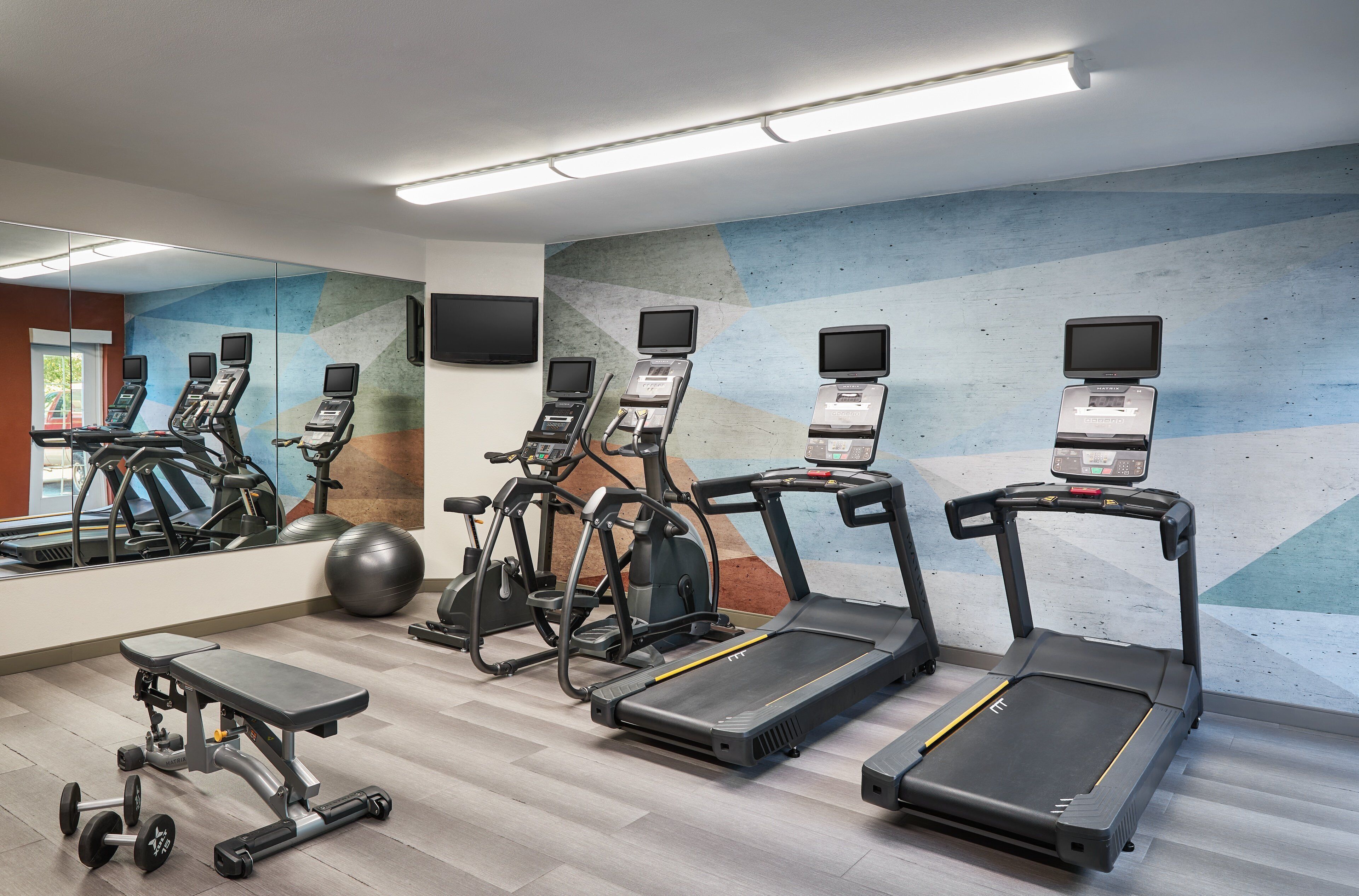 Un gimnasio con cintas de correr, elípticas y pesas libres.