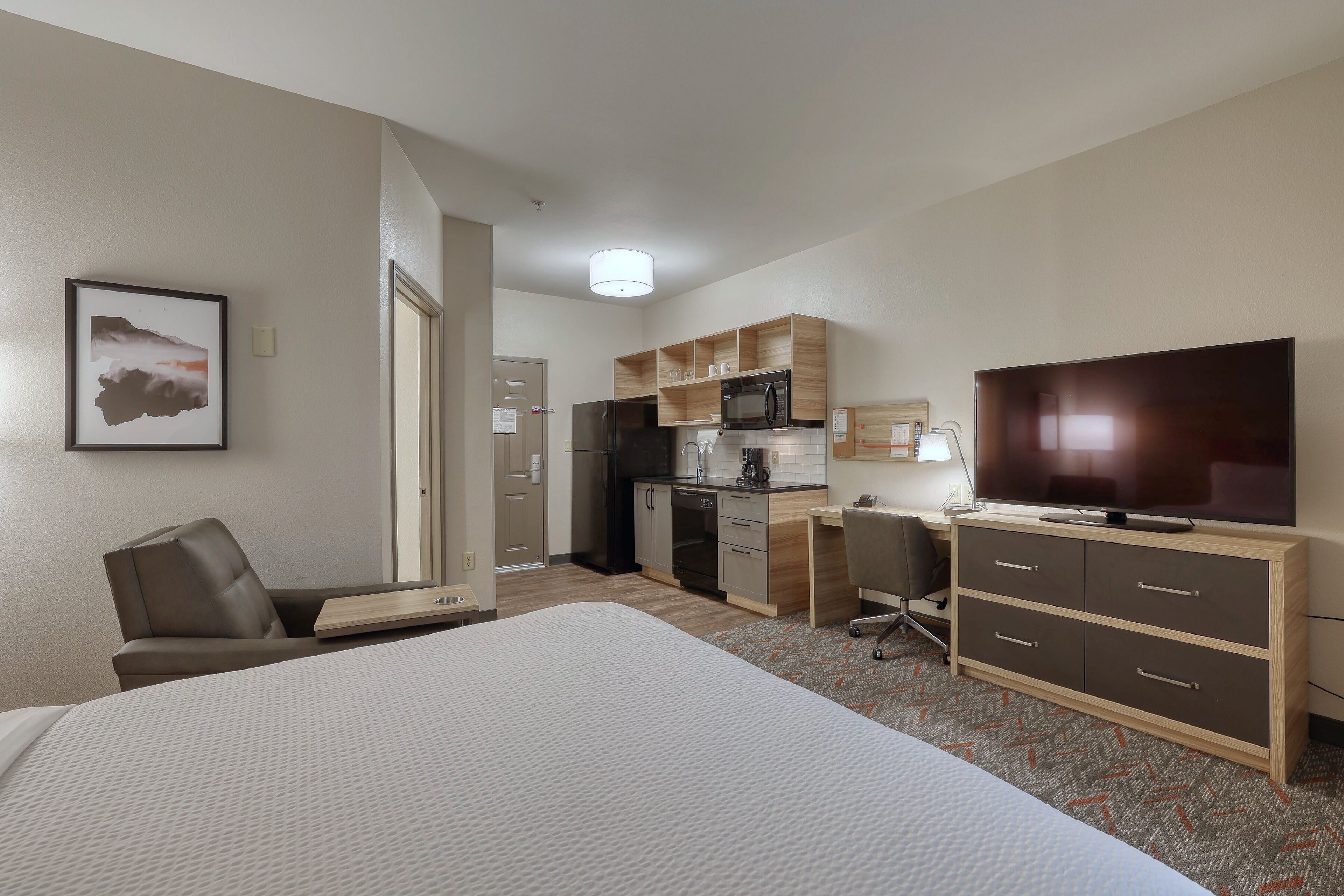 A hotel room with a bed, a desk, a chair, a television, and a kitchenette.