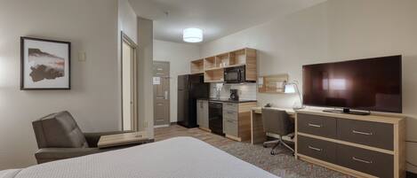 A hotel room with a bed, a desk, a chair, a television, and a kitchenette.