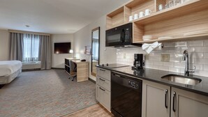 Una habitación de hotel moderna con kitchenette, una cama, un escritorio y un televisor.