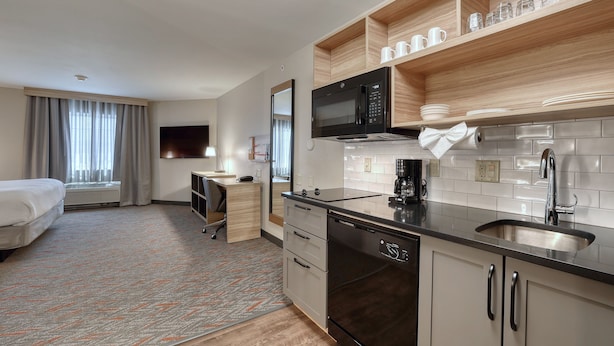 Una habitación de hotel moderna con kitchenette, una cama, un escritorio y un televisor.