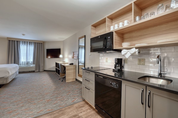 A modern hotel room with a kitchenette, a bed, a desk, and a TV.