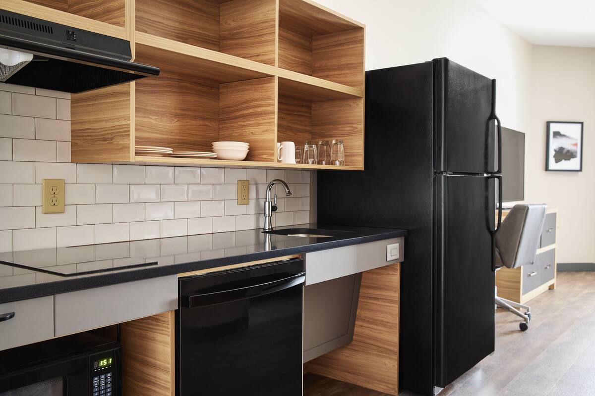 A modern kitchen with a black refrigerator, wooden shelves, a dishwasher, and a sink.
