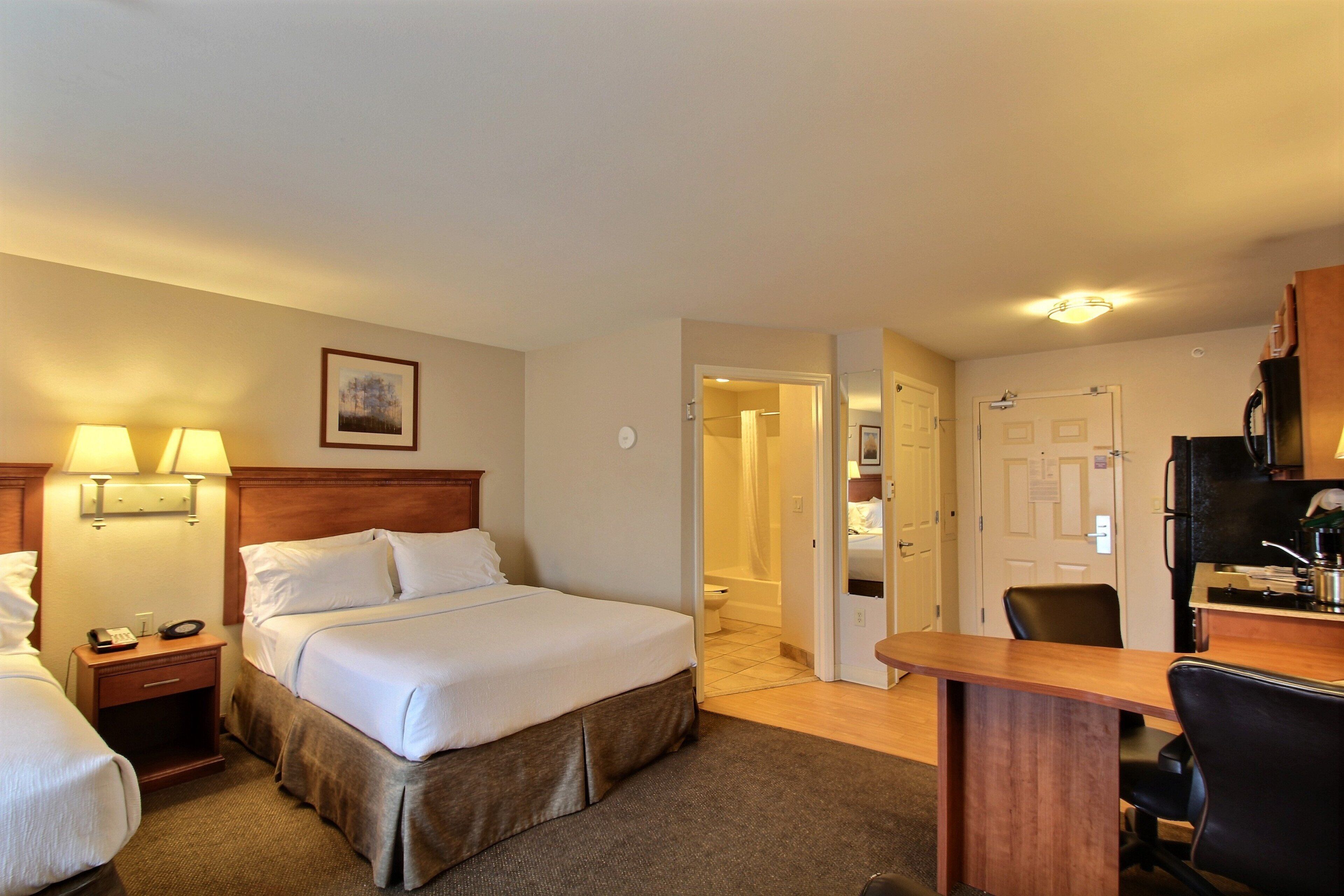 A hotel room with a bed, bedside lamps, a desk, and a chair.