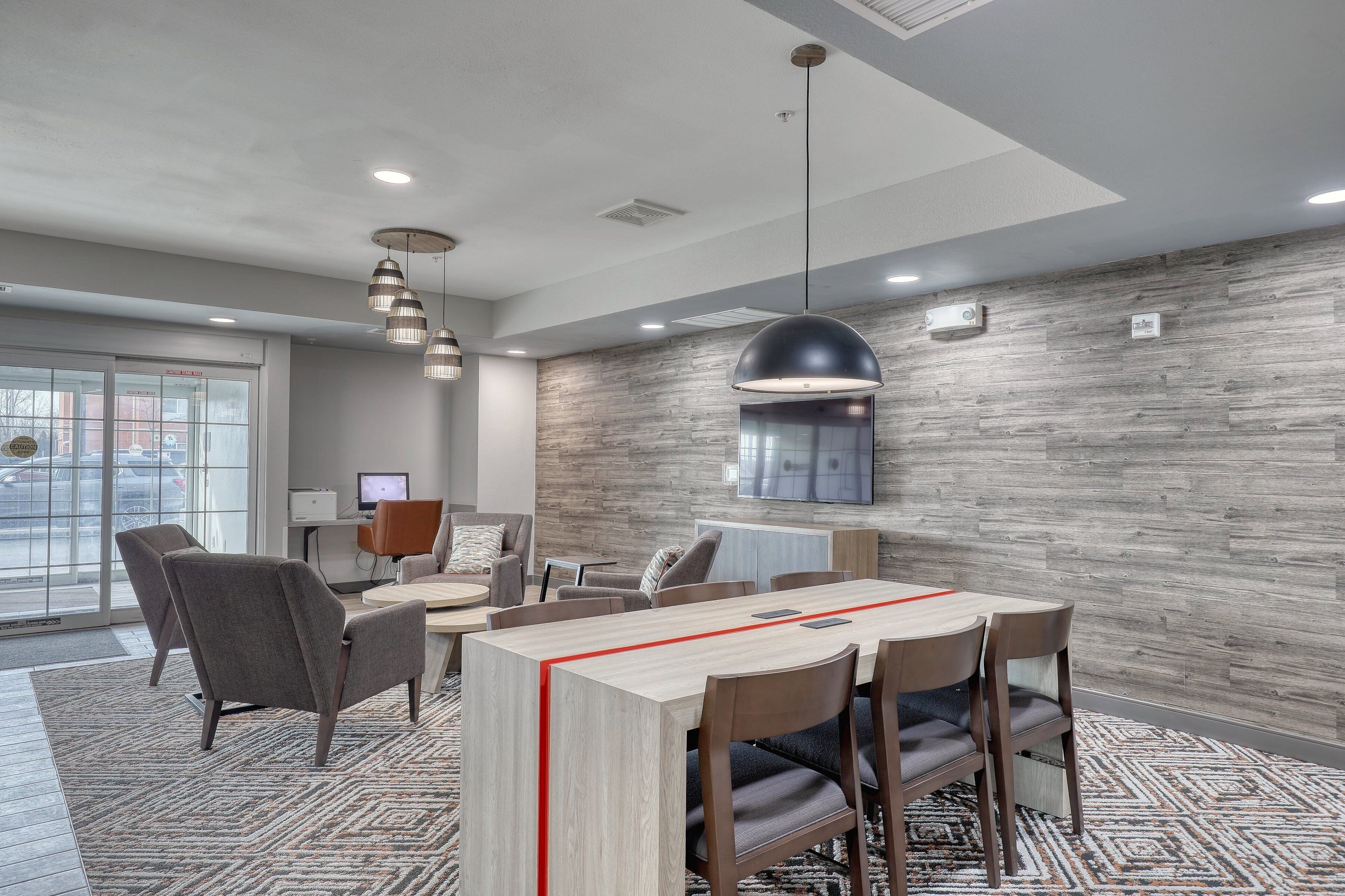 A modern conference room with a wooden table, grey chairs, and a patterned rug.