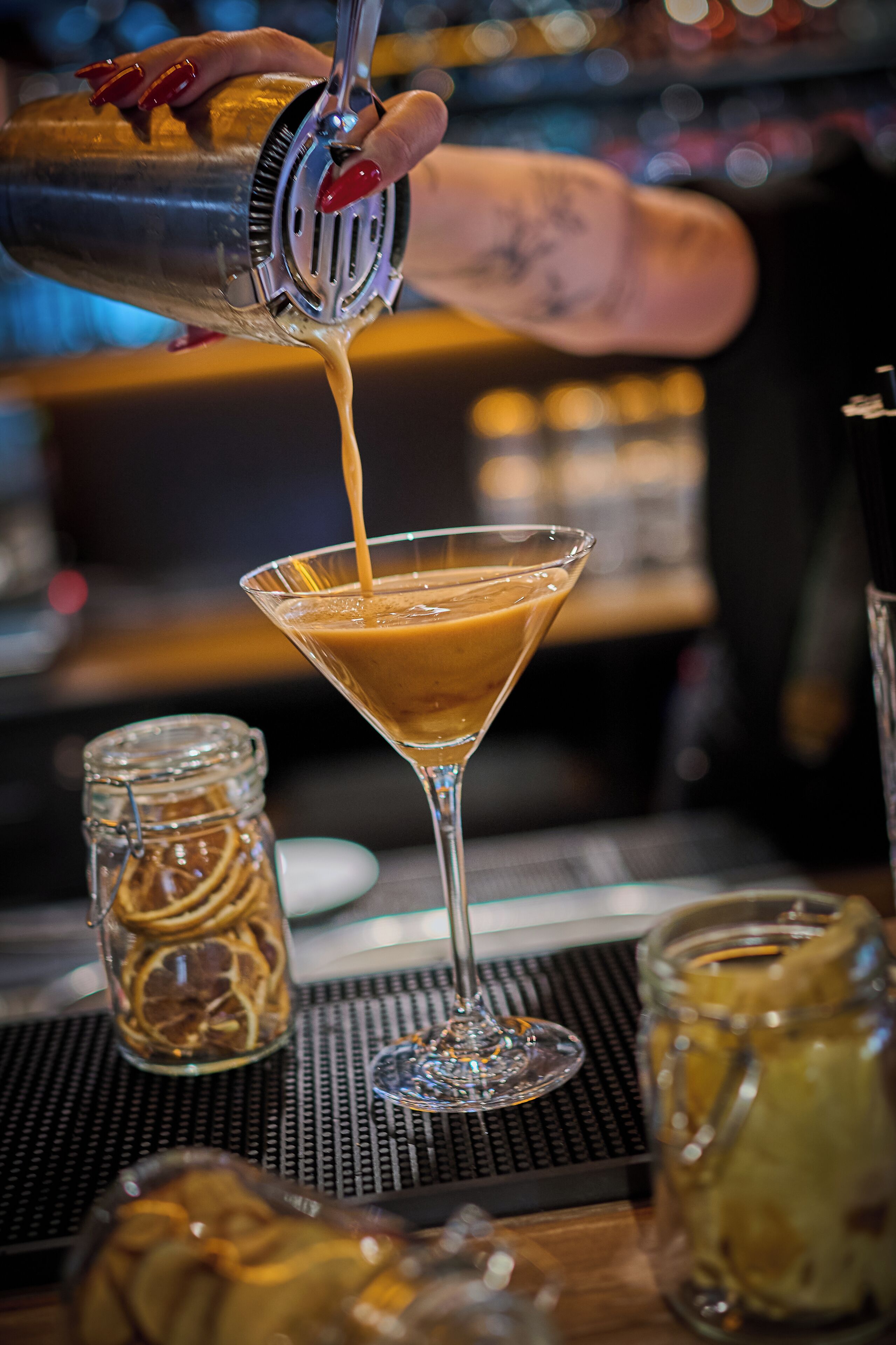 A bartender pouring a drink into a martini glass.