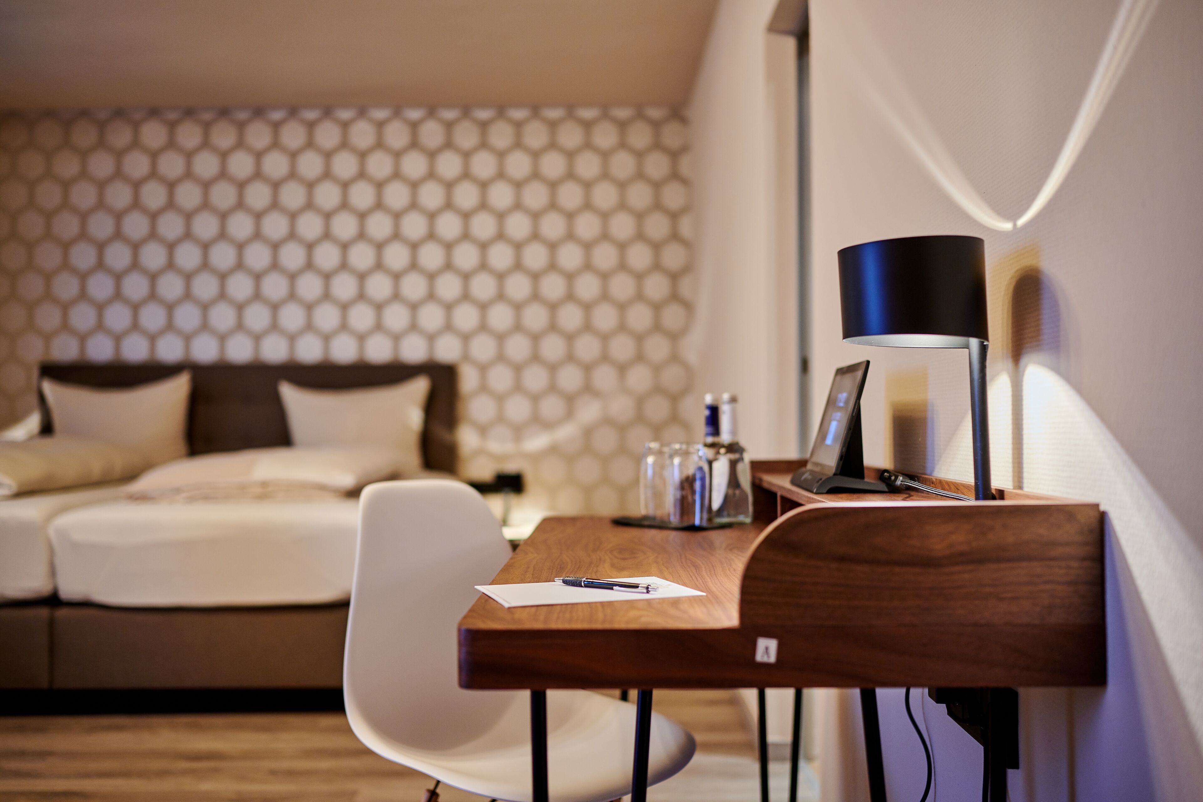 Een verzorgde hotelkamer met een bed, een bureau met lamp en een stoel.