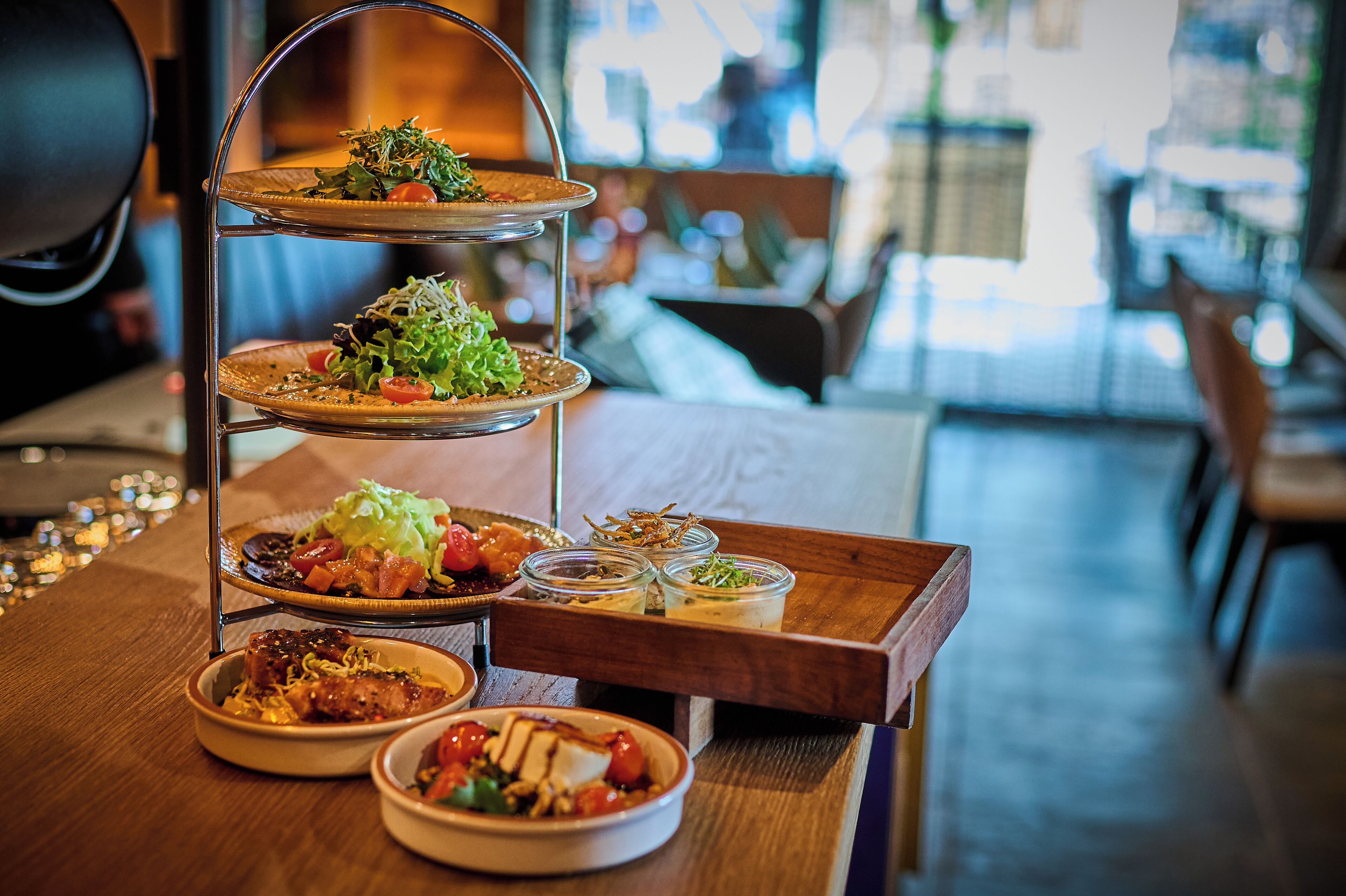A three-tiered dessert stand with various dishes on each level, placed on a wooden table in a restaurant setting.