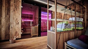 Una habitación tipo cabaña de madera con zona de ducha con paredes de cristal, una cama con toallas enrolladas y una pequeña mesa de madera con un cuenco.