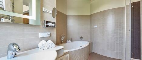 Un baño moderno con una bañera independiente, dos lavamanos, un espejo grande y un mueble de tocador con toallero.