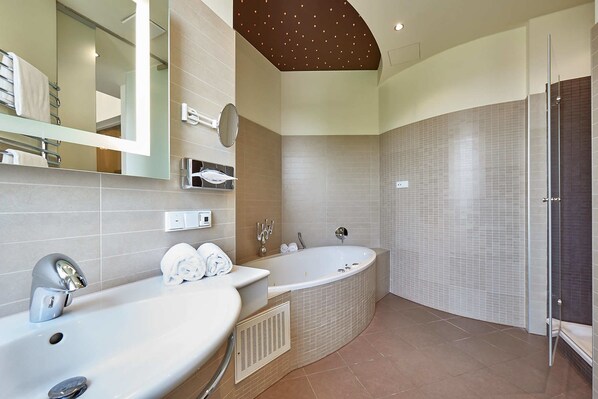 A modern bathroom with a freestanding bathtub, two sinks, a large mirror, and a vanity with a towel rack. - Genusshotel Wenisch (Straubing)