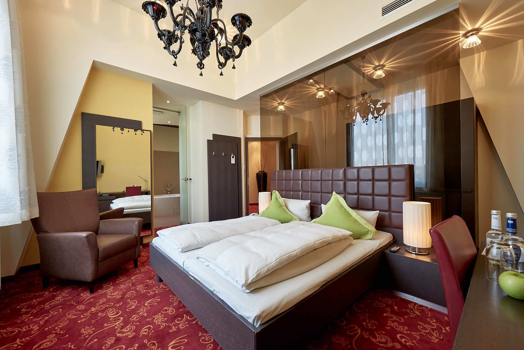 Una habitación de hotel con una cama grande, una silla, un escritorio con lámpara y un candelabro.