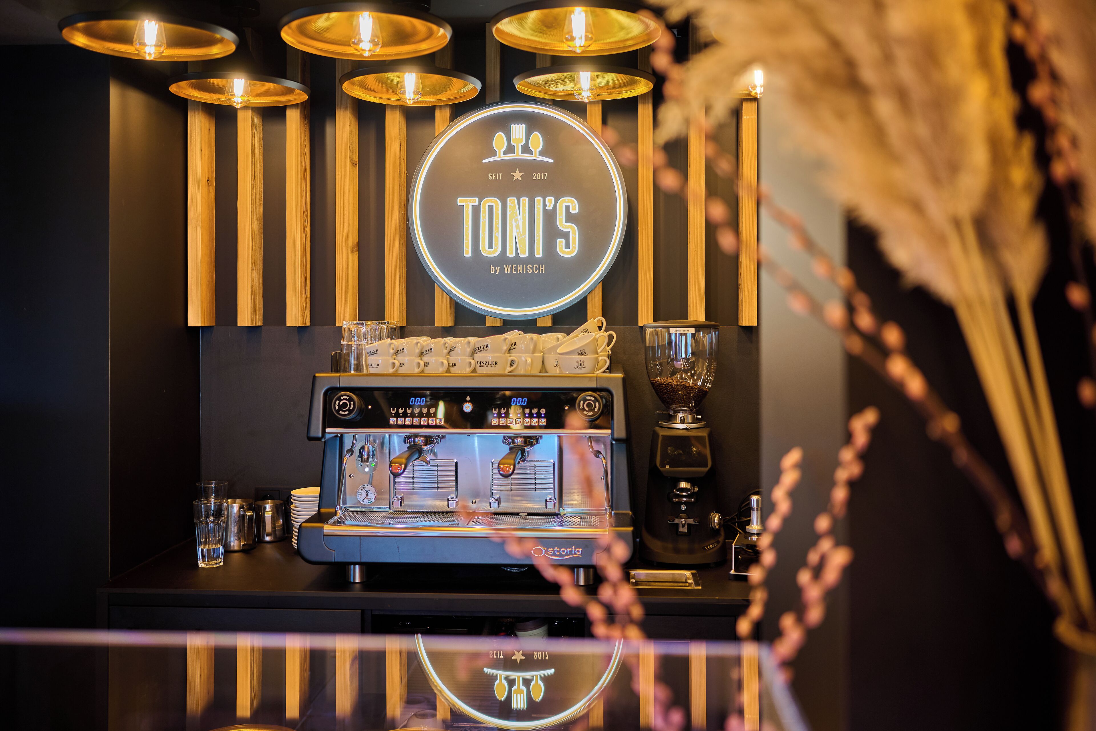 Eine Kaffeemaschine mit einem markenbezogenen Logo, ein rundes Schild darüber und vertikalen Holzleisten an der Wand.