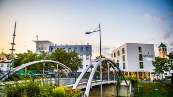 Ein modernes Hotel mit auffälligem Schild, einer Brücke mit einzigartiger Architektur und einem Kirchturm im Hintergrund.