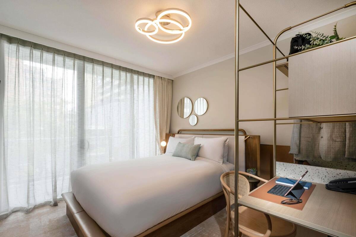 Una camera d'albergo con un letto, una scrivania con un portatile, una sedia e uno specchio.