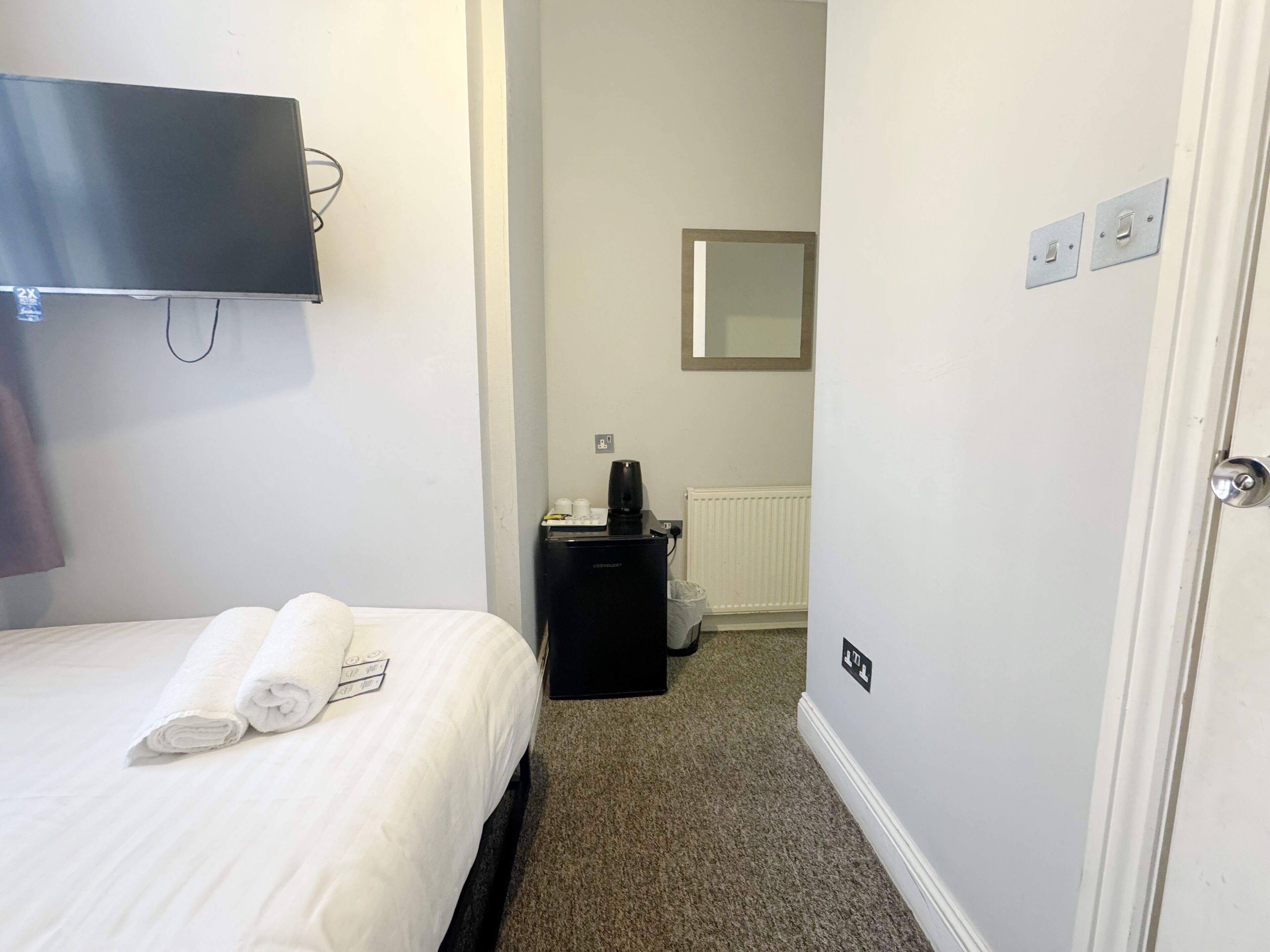 Una camera d'albergo con un letto, una TV a parete, una macchina per il caffè e un termosifone.