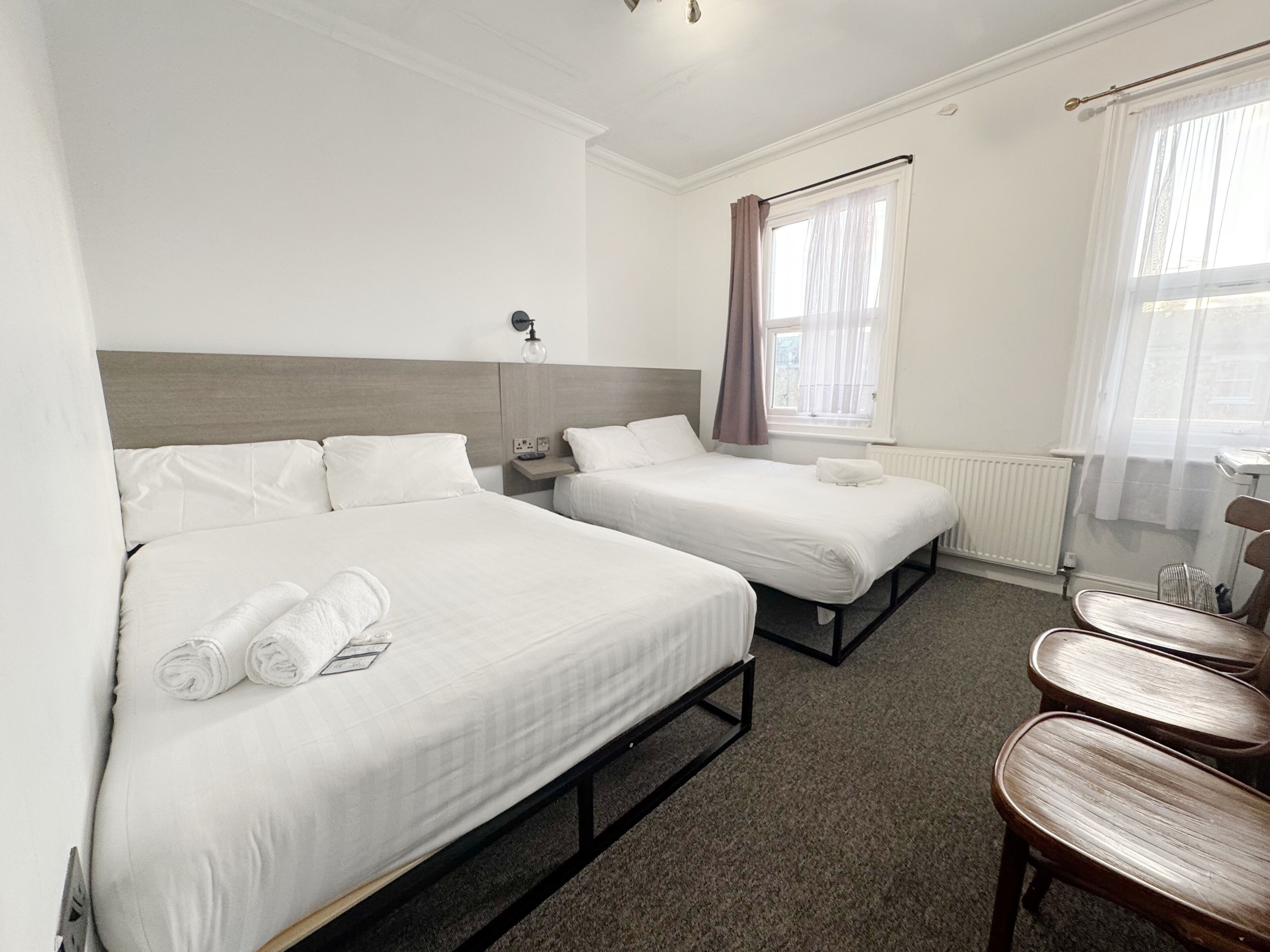 A hotel room with two beds, a nightstand, a chair, and a window with curtains.