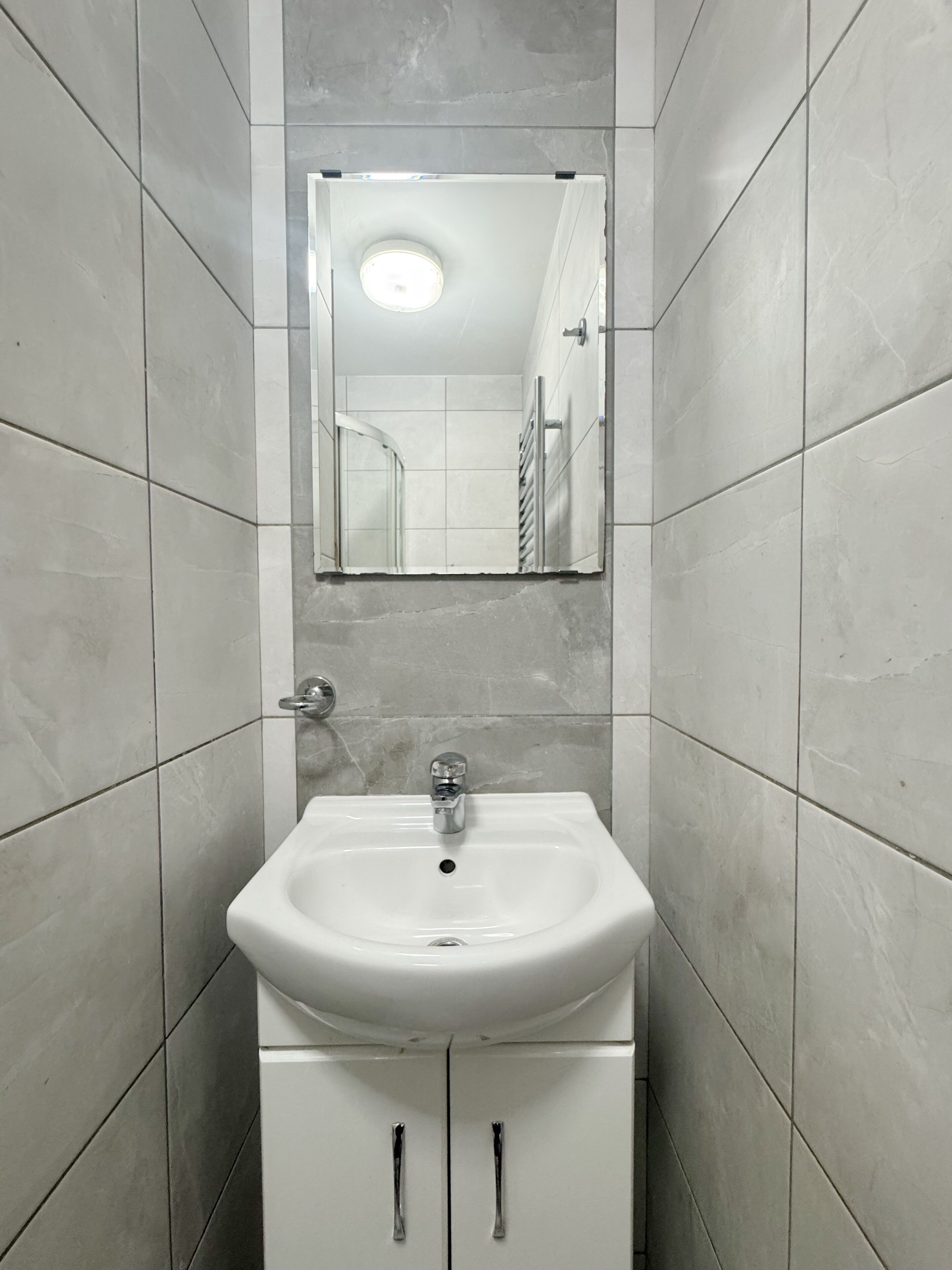 Un baño con un lavabo blanco, un espejo encima y una pared con azulejos.