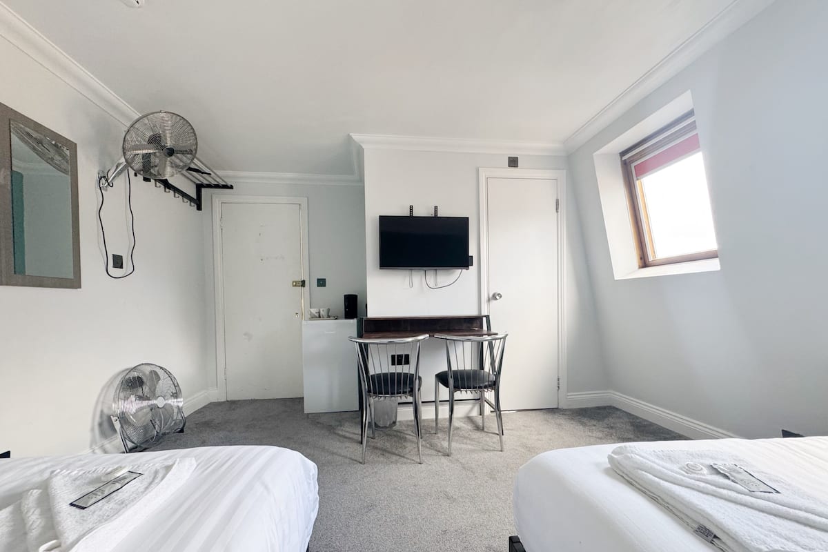 A hotel room with two beds, a desk with chairs, a television, and a window.