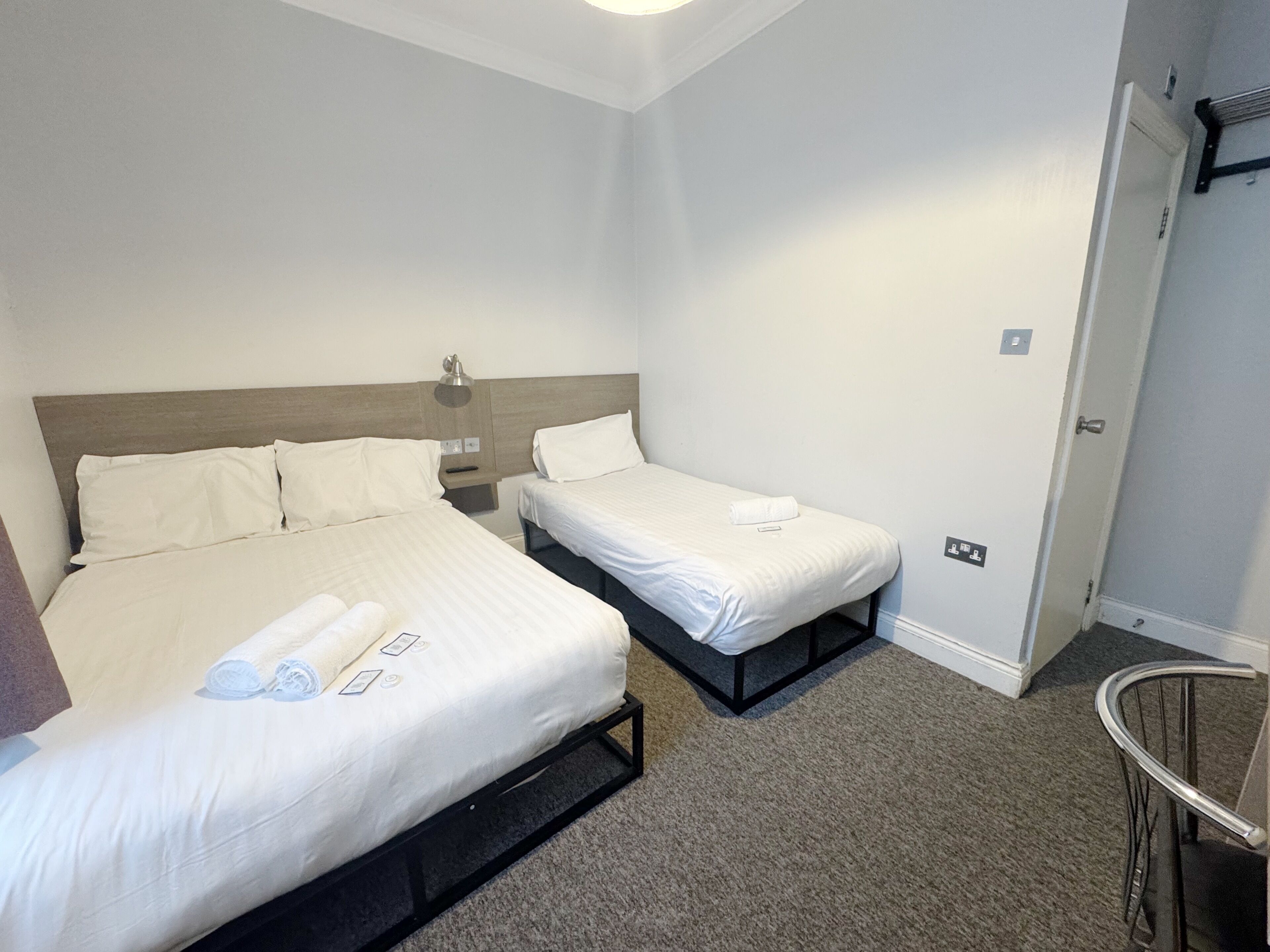 Une chambre d’hôtel avec deux lits simples, une table de chevet, une lampe, une porte et une chaise.