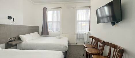 A hotel room with two beds, a TV, a desk with a lamp, and a chair.