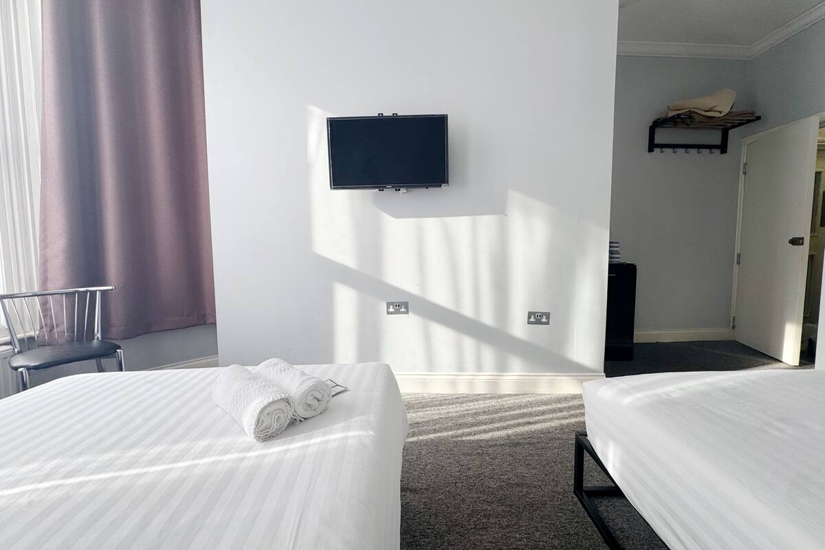A hotel room with two beds, a TV mounted on the wall, a chair, and a coat rack.