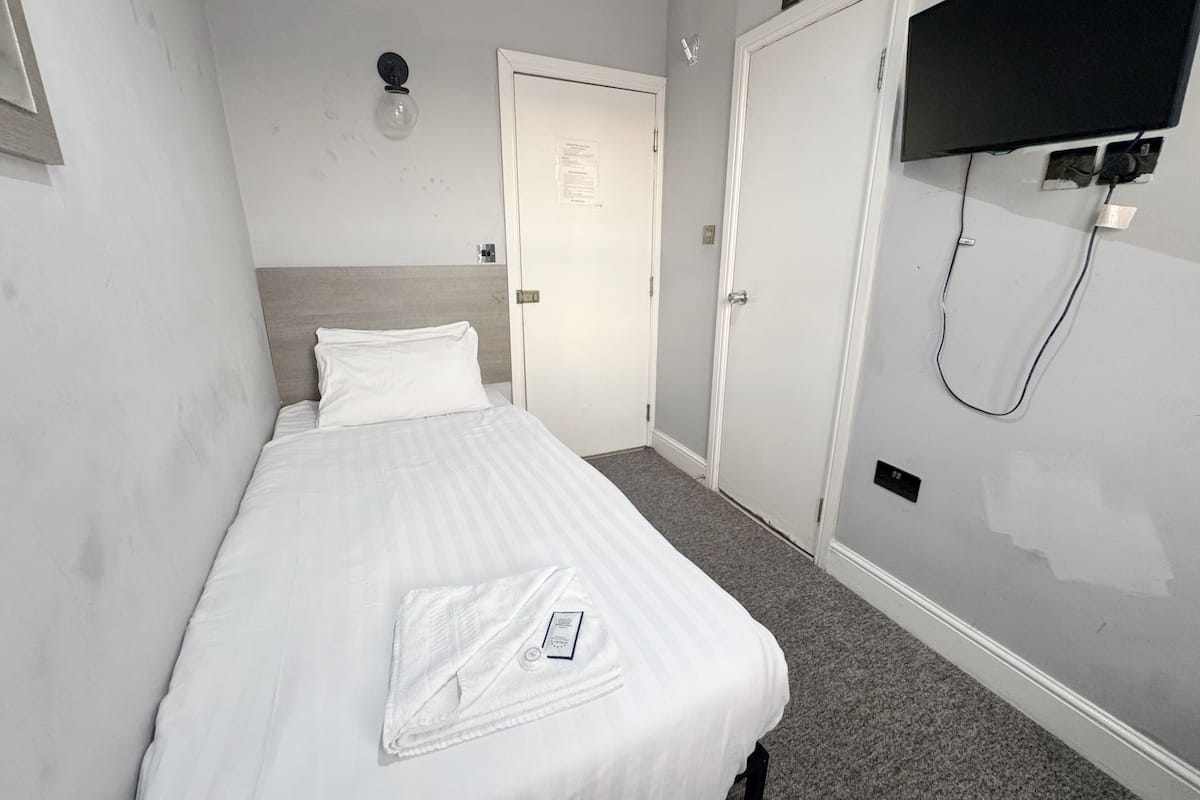 A hotel room with a bed, a flat-screen TV mounted on the wall, and a door leading to another room.