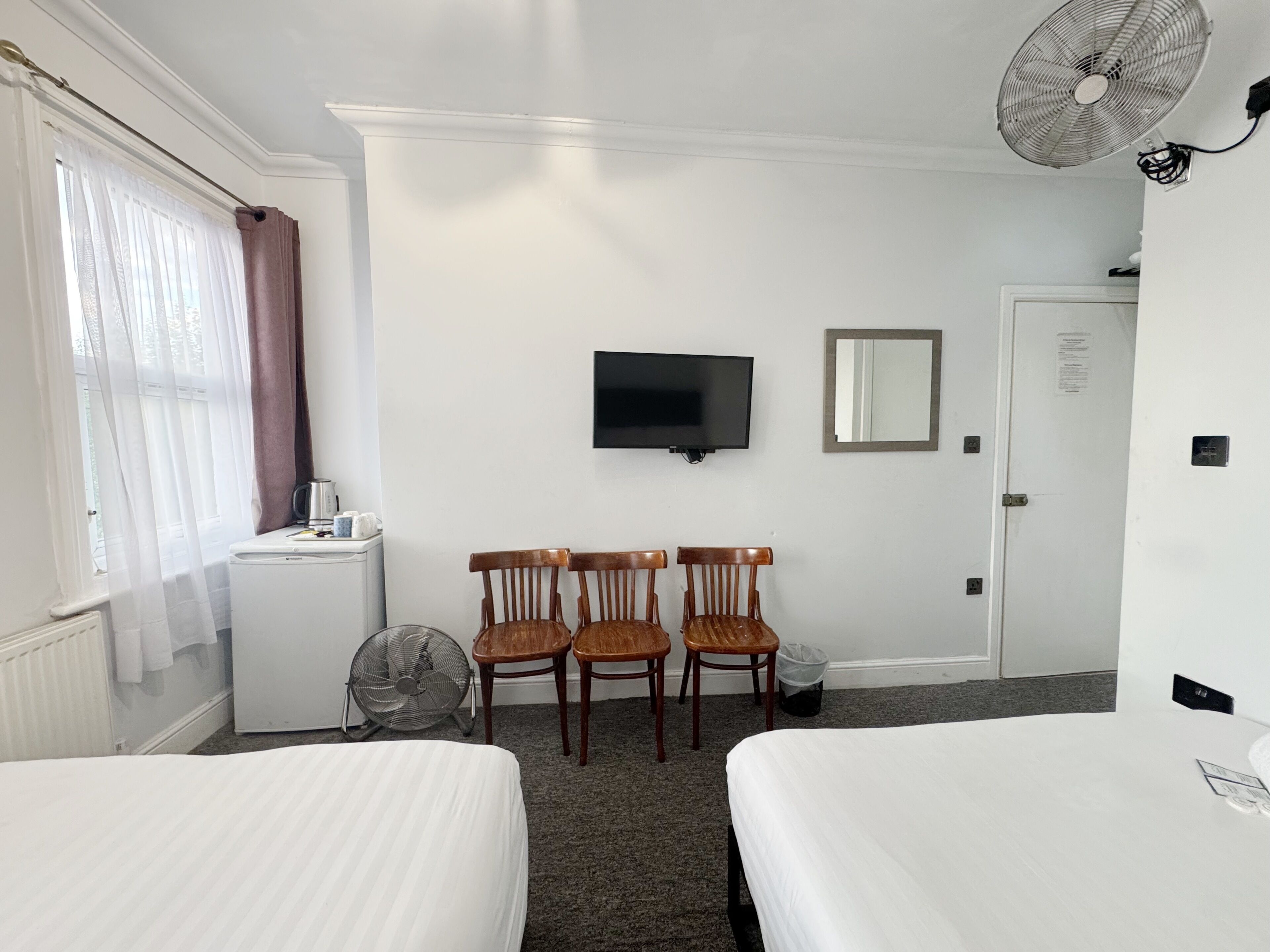 Hotelkamer met twee bedden, een televisie, een spiegel, een bureau met een ventilator en een raam met gordijnen.