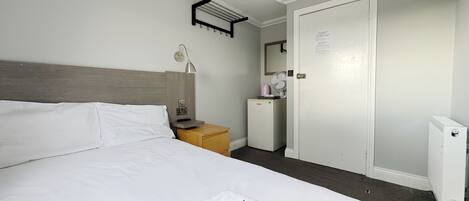 A hotel room with a bed, a bedside table with a lamp, a small refrigerator, a mirror, and a door.